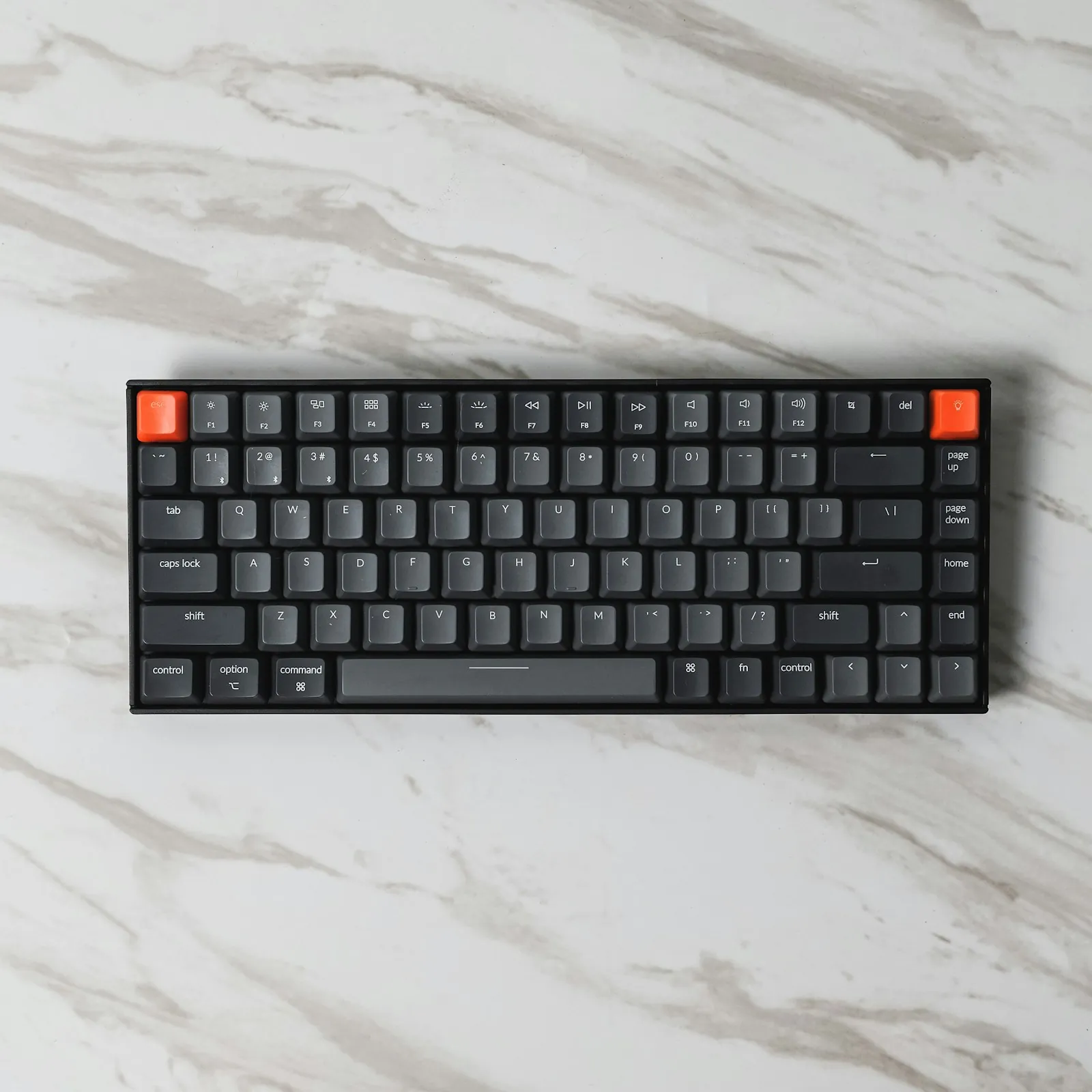 Compact mechanical keyboard with grey and orange keycaps on a marble desk